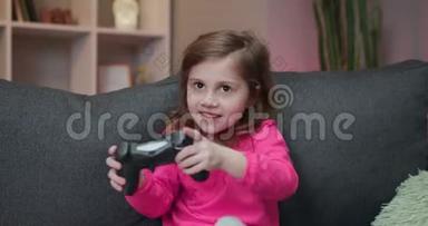 小快乐的女孩坐在沙发上，在家里的客厅里播放视频。 兴奋的玩家女孩手拿操纵杆